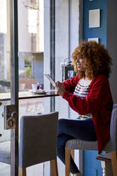 Afro-Frau lächelt, während sie in einem Café sitzt und ein digitales Tablet benutzt - VEGF03679