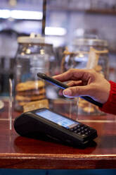 Frau benutzt Mobiltelefon zum Bezahlen in einem Cafe - VEGF03690