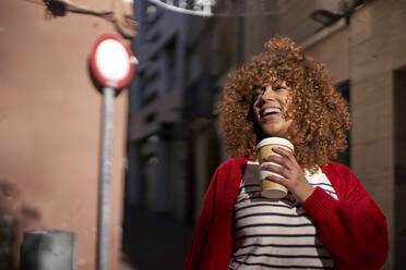 Smiling woman with disposable coffee cup looking away while standing outdoors - VEGF03711