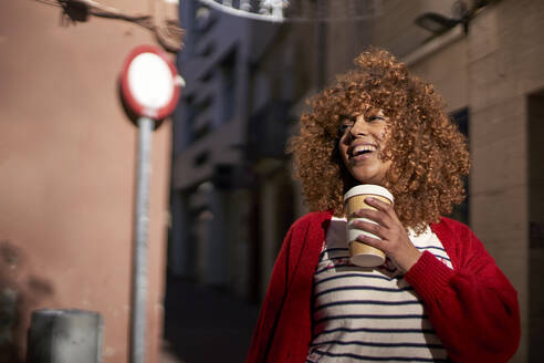 Lächelnde Frau mit Einweg-Kaffeetasse, die im Freien steht und wegschaut - VEGF03711