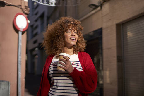 Schöne Frau mit Einweg-Kaffeebecher lächelnd, während gegen Straße stehen - VEGF03712