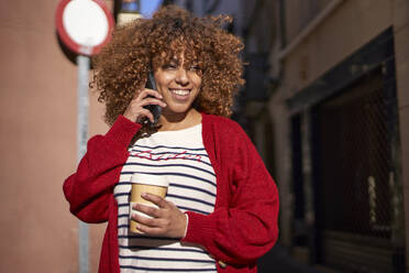 Lächelnde Frau, die wegschaut, während sie im Freien stehend mit ihrem Handy telefoniert - VEGF03716