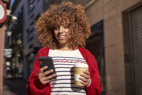Afro-Frau mit Einwegbecher, die im Freien stehend ein Mobiltelefon benutzt - VEGF03717