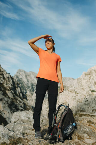 Frau schirmt die Augen ab, während sie auf einem Berg am Cares Trail im Nationalpark Picos De Europe, Asturien, Spanien, steht und die Aussicht betrachtet, lizenzfreies Stockfoto