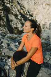 Smiling woman admiring view while sitting on mountain at Cares Trail in Picos De Europe National Park, Asturias, Spain - DMGF00451