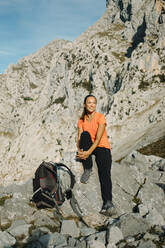 Frau mit Rucksack, die sich auf einem Felsen sitzend auf dem Cares Trail im Nationalpark Picos De Europe, Asturien, Spanien, ausruht - DMGF00452