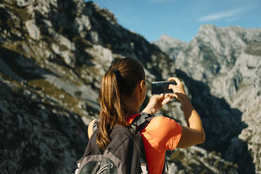 Hiker taking photo through mobile phone while standing at Cares Trail in Picos De Europe National Park, Asturias, Spain - DMGF00463