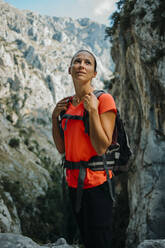 Weibliche Forscherin mit Rucksack, die wegschaut, während sie am Cares Trail im Nationalpark Picos De Europe, Asturien, Spanien steht - DMGF00468