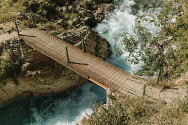 Holzbrücke über einen fließenden Fluss am Cares Trail im Nationalpark Picos De Europe, Asturien, Spanien - DMGF00470