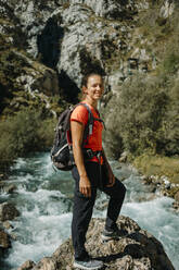 Lächelnde Frau mit Rucksack, die am Cares Trail im Nationalpark Picos De Europe, Asturien, Spanien, am Fluss steht - DMGF00472
