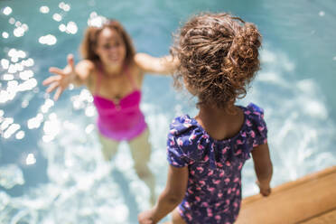 Daughter preparing to jump into arms of mother in sunny swimming pool - CAIF30308