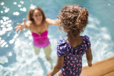 Tochter bereitet sich auf einen Sprung in die Arme der Mutter im sonnigen Schwimmbad vor - CAIF30308