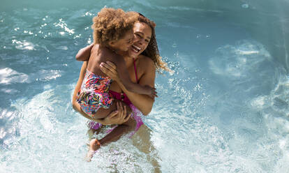 Glückliche Mutter hält ihre Tochter im sonnigen Sommerschwimmbad - CAIF30309