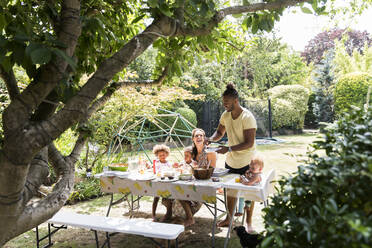 Father serving barbecue to family at summer backyard table - CAIF30311