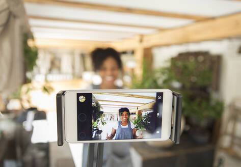 Female shop owner filming vlog with smart phone in plant nursery - CAIF30318