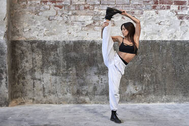Weibliche Tänzerin steht auf einem Bein vor einer verwitterten Wand in einer Fabrik - VEGF03723