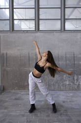 Verführerische Tänzerin mit ausgestreckten Armen tanzt gegen die Wand in einer verlassenen Fabrik - VEGF03729