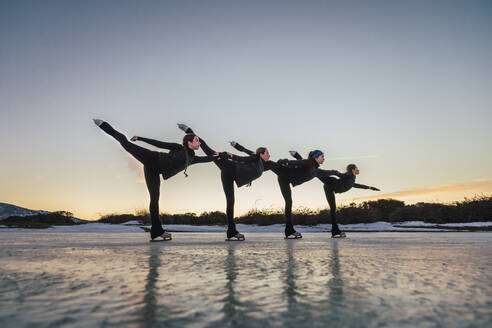 Female figure skaters practicing on frozen lake at dusk - RSGF00531