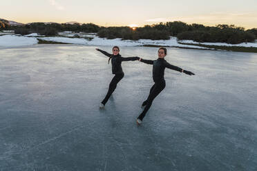 Zwei Eiskunstläuferinnen üben gemeinsam auf einem zugefrorenen See in der Abenddämmerung - RSGF00537