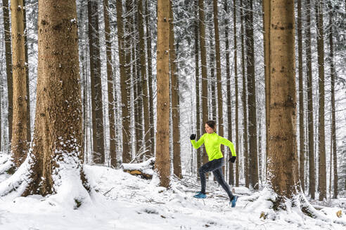 Weibliche Athletin läuft im Winter zwischen Bäumen - STSF02806