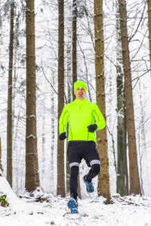 Männlicher Athlet, der im Winter auf Schnee im Wald läuft - STSF02808