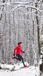 Weibliche Sportlerin läuft im Winter über einen verschneiten, umgestürzten Baum - STSF02812