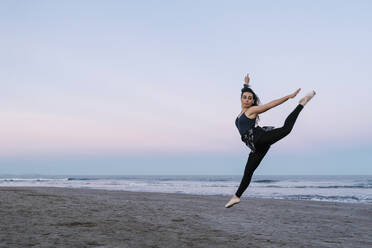 Flexible female dancer with legs apart practicing at beach against sky - EGAF01654