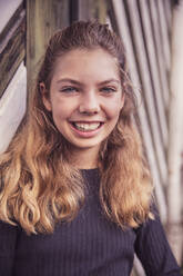 Smiling girl staring while standing against barn door - DHEF00516