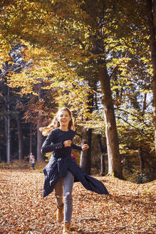 Lächelndes Mädchen läuft im Herbst im Wald - DHEF00532