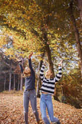 Mädchen werfen ein trockenes Blatt beim Spielen im Wald - DHEF00533