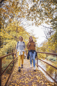 Frauen lächelnd beim Spaziergang auf einer Brücke im Wald - DHEF00535