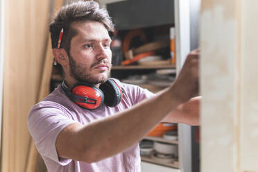 Male craftsperson with ear protectors working in workshop - JAQF00209