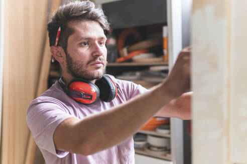 Männlicher Handwerker mit Gehörschutz bei der Arbeit in der Werkstatt - JAQF00209