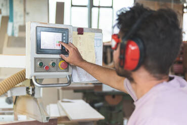 Male carpenter operating machine while working in workshop - JAQF00220