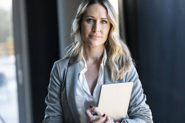 Confident businesswoman holding digital tablet while standing at office - JSRF01337