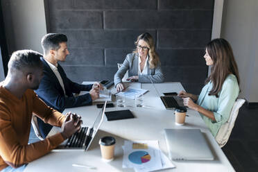 Business people discussing over document while sitting in meeting at office - JSRF01338