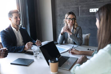 Lächelnde Geschäftsleute, die im Büro sitzen und diskutieren - JSRF01340