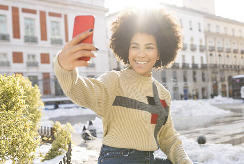 Afro Frau lächelnd bei der Aufnahme von Selfie durch Handy sitzen in der Stadt - JCCMF01069