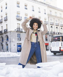 Smiling woman wearing jacket standing with hand raised on road - JCCMF01075