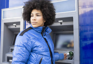 Frau schaut weg, während sie an der Bushaltestelle ein Ticket aus dem Automaten zieht - JCCMF01100