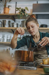 Expertise adding seasoning while cooking broth in copper saucepan standing in kitchen - MFF06978