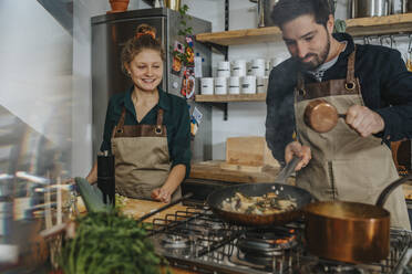 Junger Koch, der in der Küche steht und auf sein Fachwissen beim Kochen von Austernpilzen in der Bratpfanne schaut - MFF06991