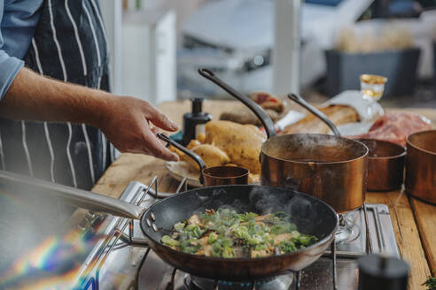 Männliches Fachwissen beim Kochen von Austernpilzen und Frühlingszwiebeln in einer Bratpfanne, während man in der Küche steht - MFF06995