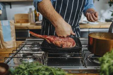 Koch prüft rohes Tomahawk-Steak in der Bratpfanne, während er in der Küche steht - MFF07004