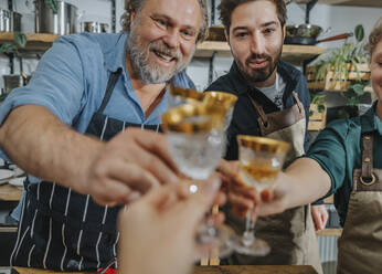 Chefs toasting drinks with woman drinking glass while standing in kitchen - MFF07020