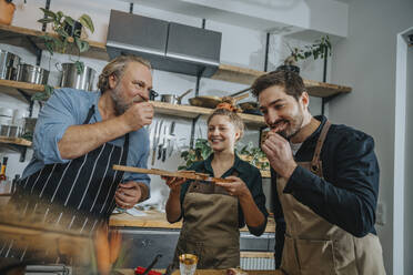 Male chefs tasting salami while standing by colleague in kitchen - MFF07022