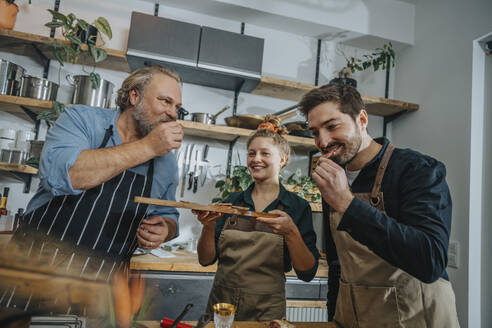 Männliche Köche probieren Salami, während sie neben einem Kollegen in der Küche stehen - MFF07022