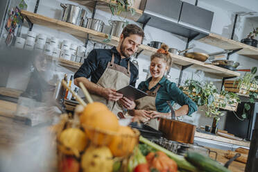 Mid adult chef using digital tablet while standing by colleague in kitchen - MFF07042