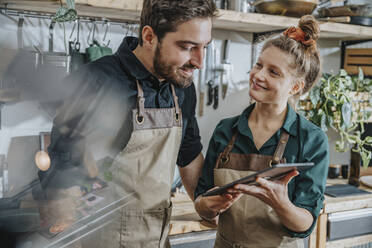 Smiling chef using digital tablet while standing by colleague in kitchen - MFF07043