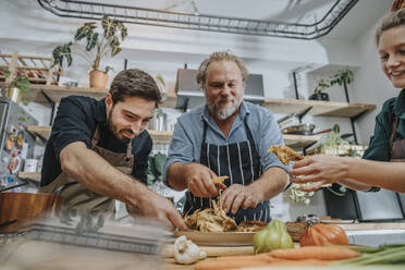 Smiling chefs taking cooked meat while standing in kitchen - MFF07054